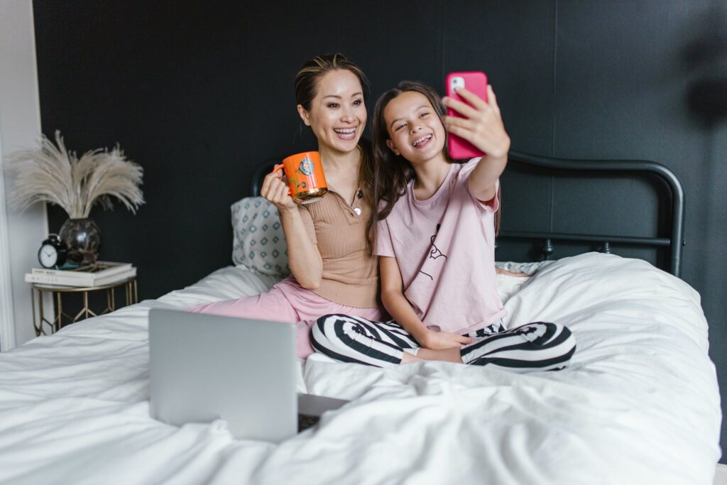 A Young Girl Taking Selfie with Her Mother while Sitting on the Bed